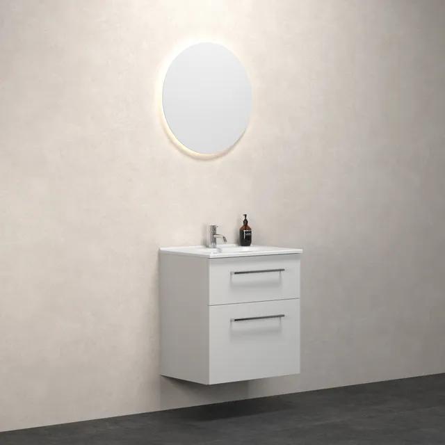 Väggmonterat badrumsskåp med två lådor, ovanför en rund spegel med belysning. En liten flaska står på skåpet.