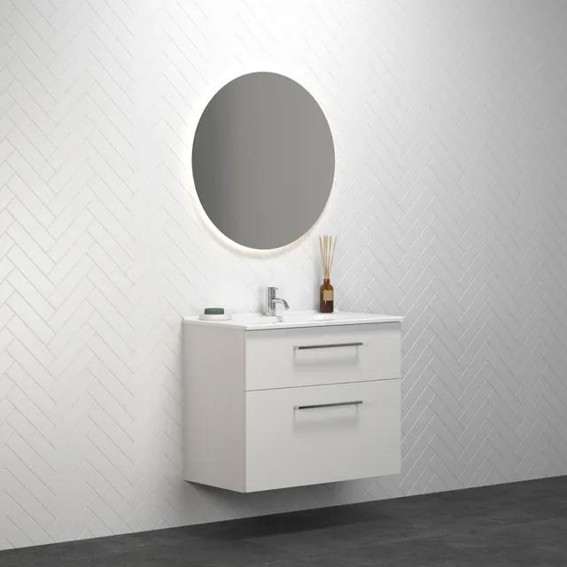 Vitt badrumsmöbelset med två lådor, rund spegel och belysning. Vägg i vit kakel med fiskbensmönster.