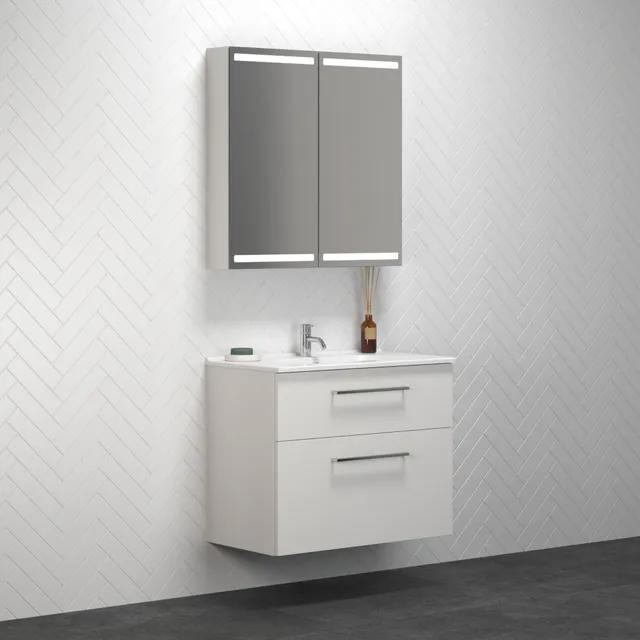 Vitt spegelskåp med belysning och vit kommod med två lådor, placerad mot ett vitt fiskbensmönstrat kakel.