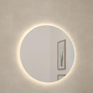 Rund spegel med bakgrundsbelysning på en beige vägg, reflekterar tavlor med växtmotiv.