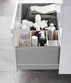 Öppen låda med olika flaskor och behållare, handdukar och föremål i separata fack. Grått klinkergolv.