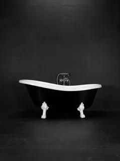 Svart badkar med vit insida och vita tassformade ben mot en mörk kaklad vägg.