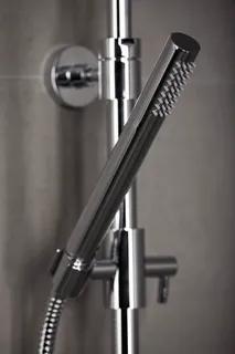 Kromfärgad duschhandtag med rund design och flexibel slang, monterad mot grått kakel.