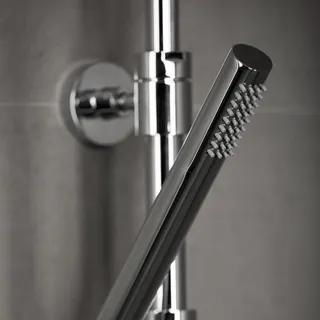 Duschhuvud av metall med borstliknande munstycken på en stång mot en grå vägg.