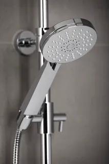 Duschmunstycke i krom med väggfäste och slang mot en grå kaklad vägg.